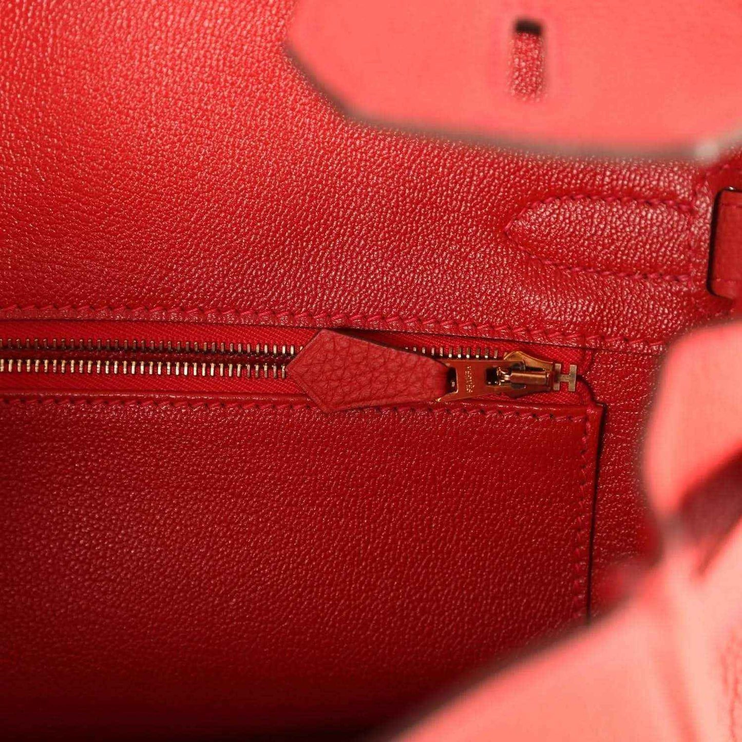 Elegant red leather handbag interior with gold zipper, showcasing timeless sophistication.