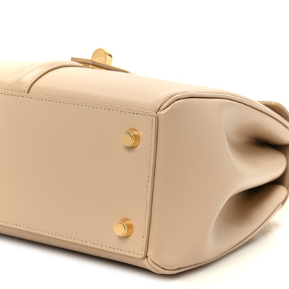 Nude small top-handle bag with curved flap edge and gold snap hardware