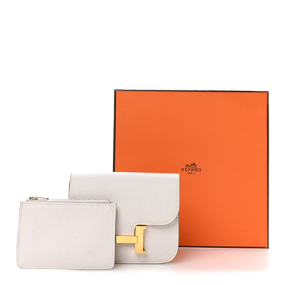 Pale gray slim wallet with gold H clasp next to Hermes presentation box.