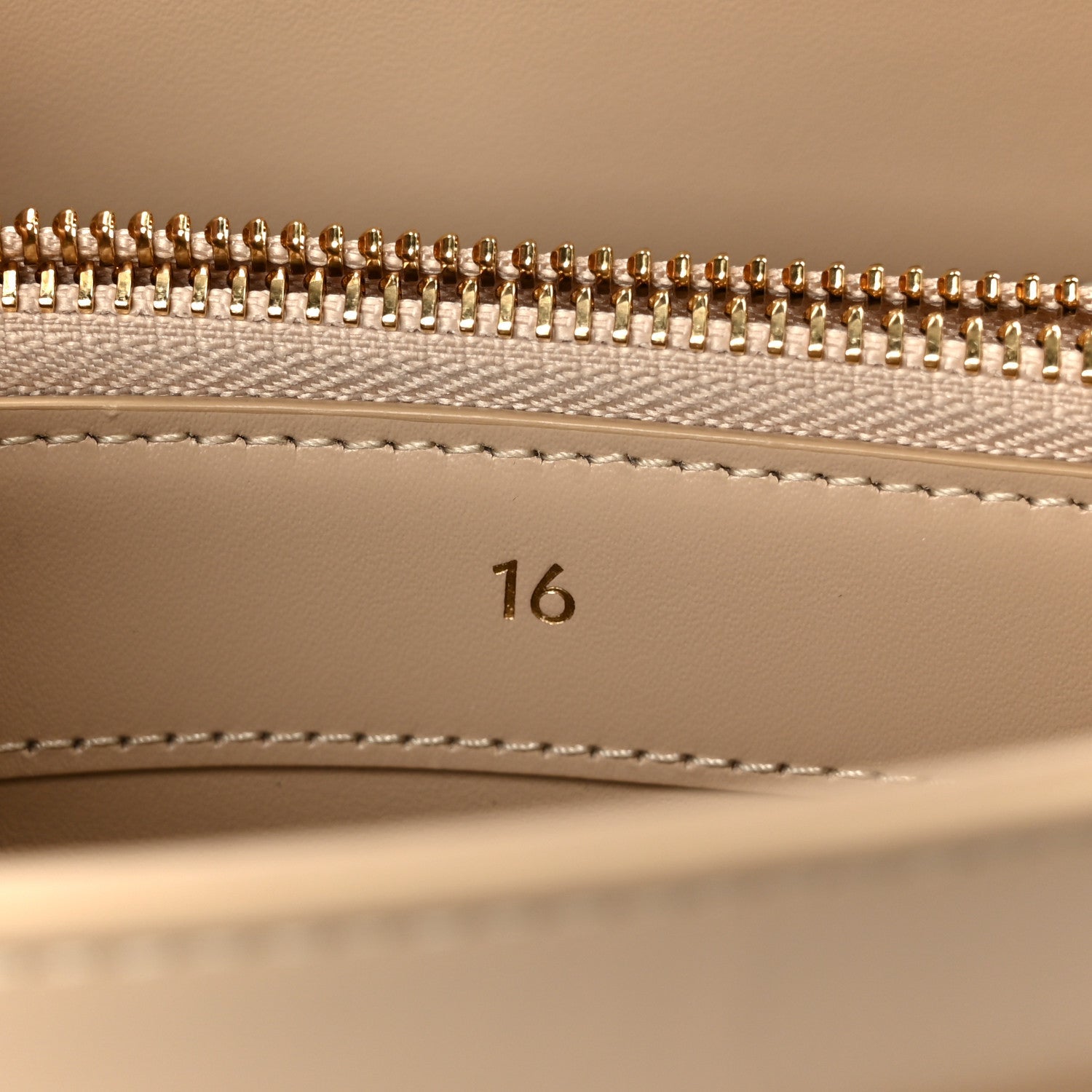 Gold zipper teeth and beige lining with stitched seam inside a small bag