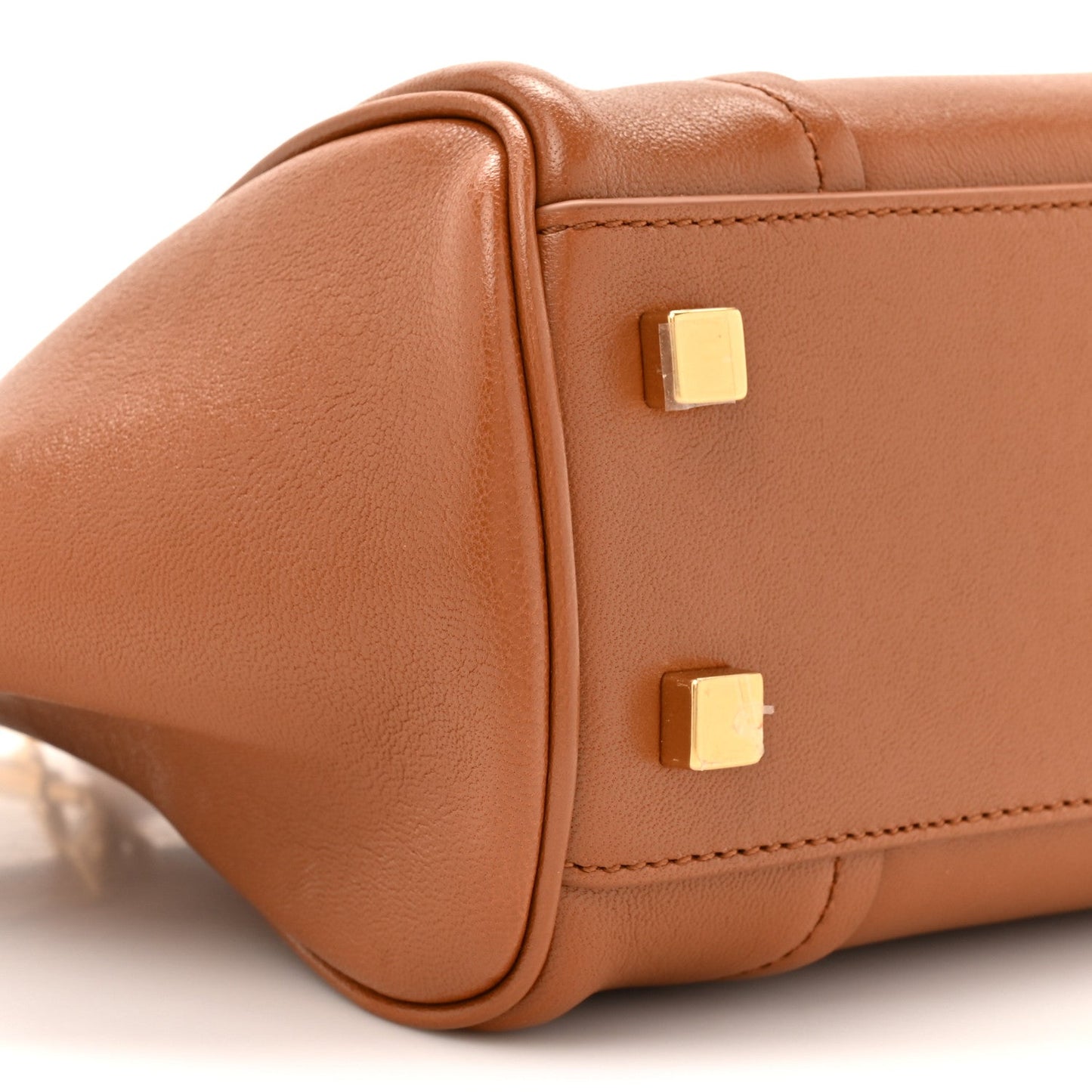 Tan leather handbag corner with gold-tone stud hardware and curved edge stitching.