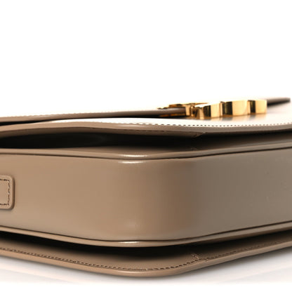 Shiny brown leather shoulder bag with gold-tone top trim and curved flap edge