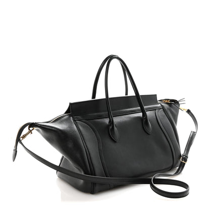 Black leather luggage bag with crossbody strap and gold zip pulls.