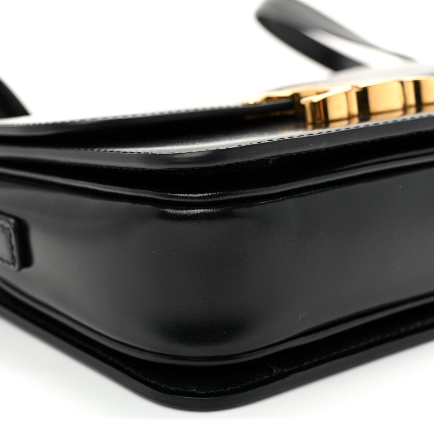 Close-up of black bag corner with gold-tone clasp and smooth curved flap edge.