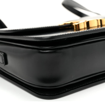 Close-up of black bag corner with gold-tone clasp and smooth curved flap edge.