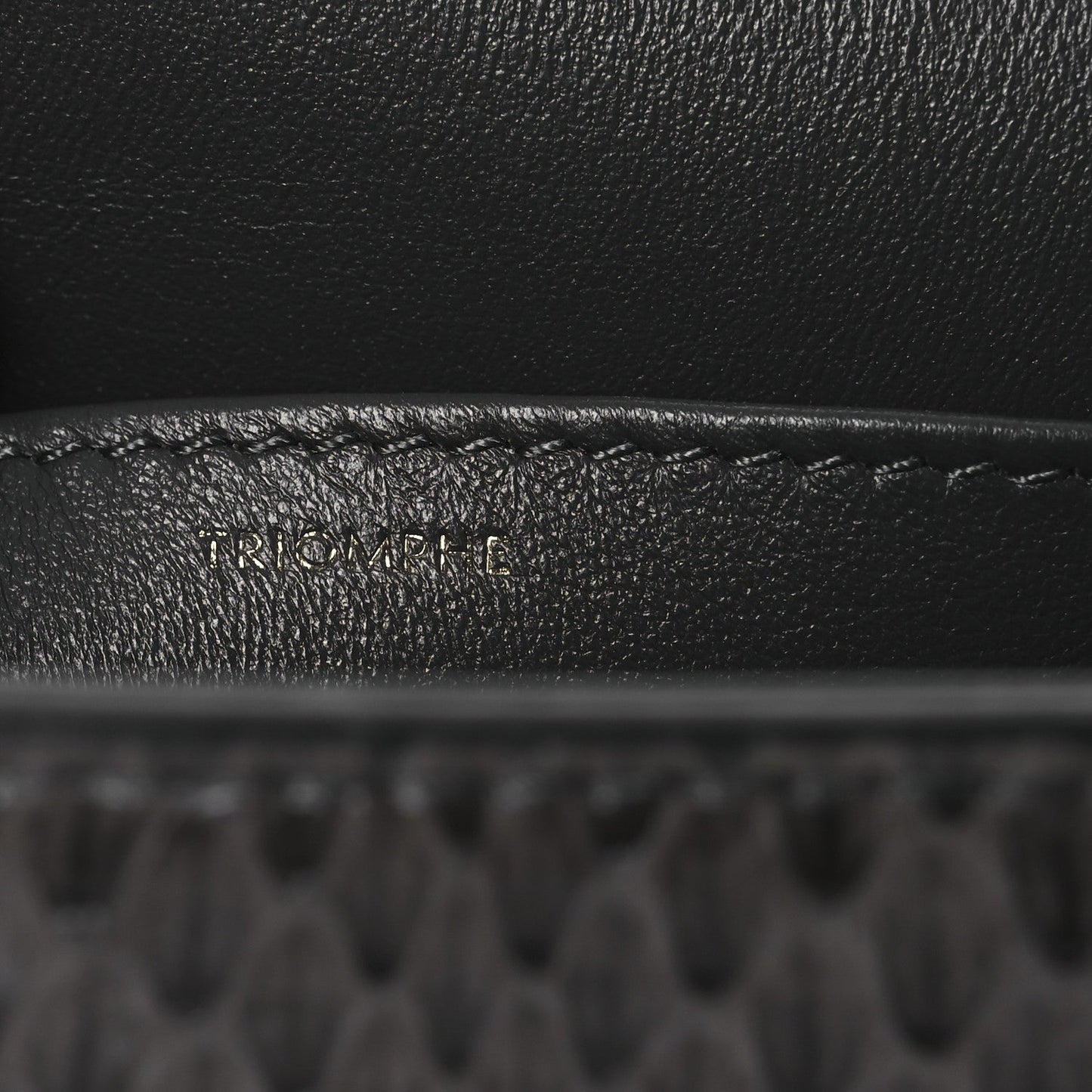 Grey snakeskin shoulder bag flap close-up with embossed brand detail