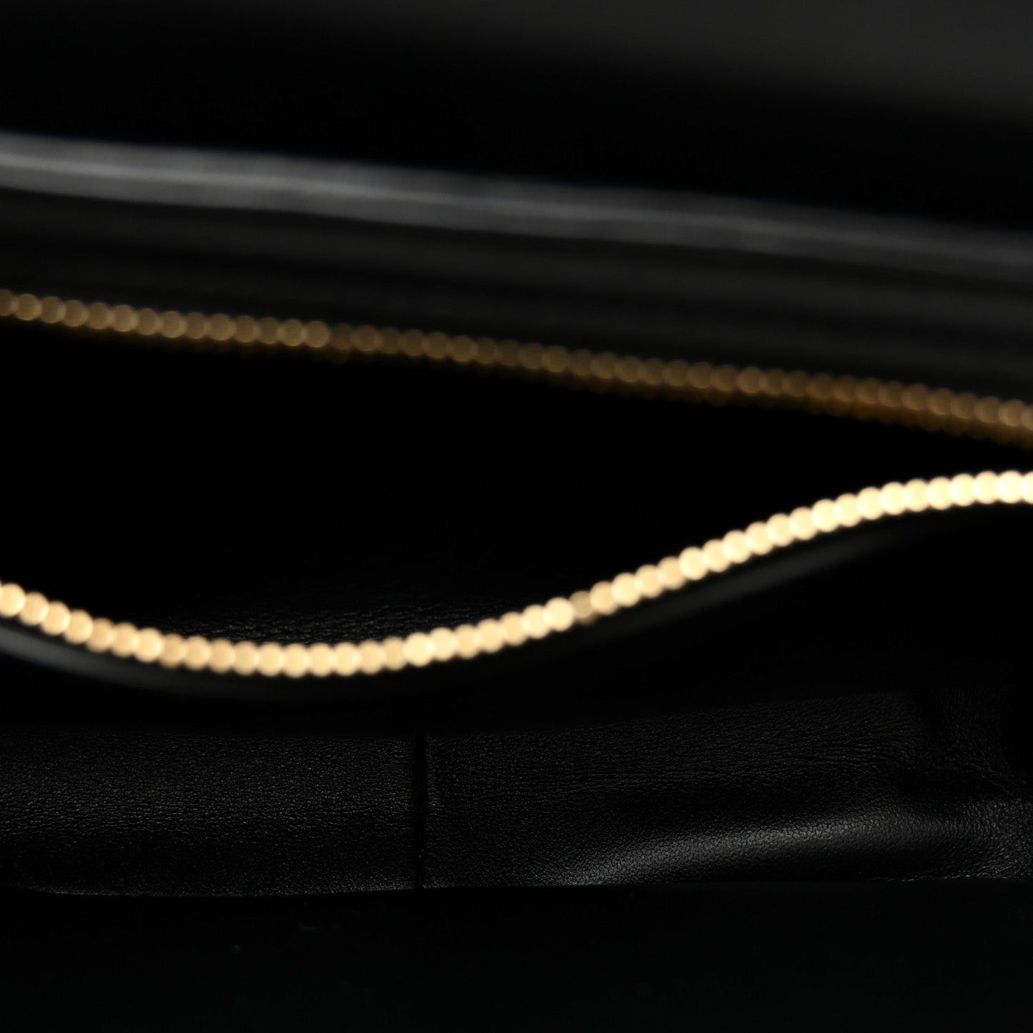 Close-up of black leather bag interior edge with gold chain trim.