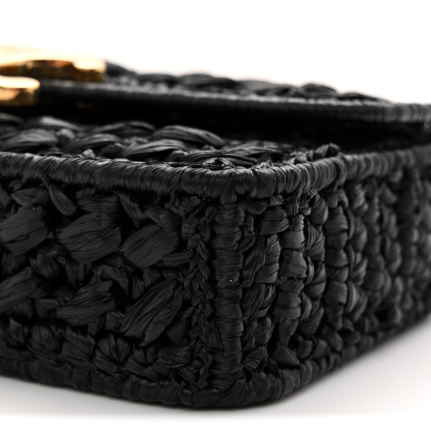 Black woven raffia-effect bag side with out-of-focus chain hardware