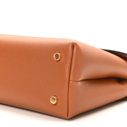 Tan leather handbag corner close-up with two gold snap buttons and curved base edge