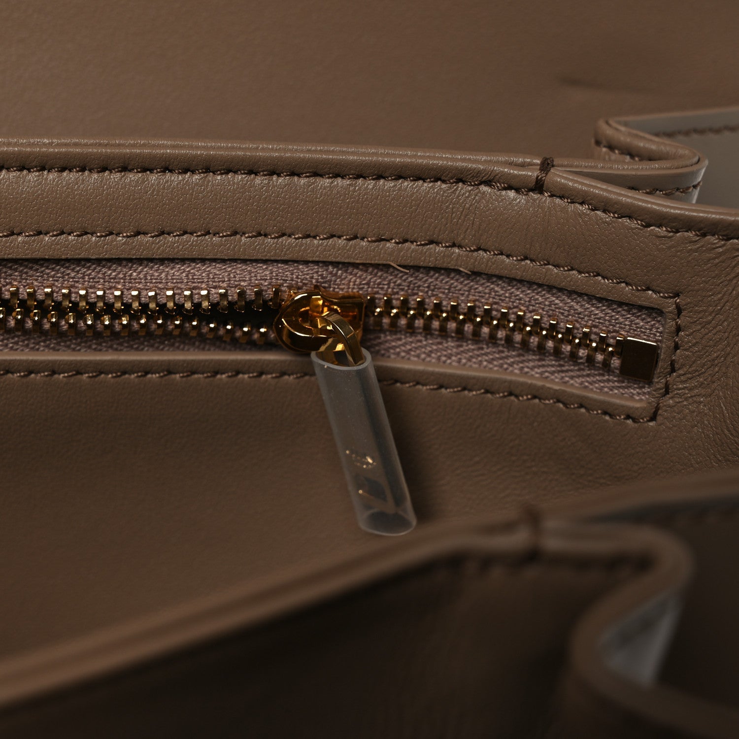 Shiny brown leather bag close-up of gold-tone zipper and clear zip pull