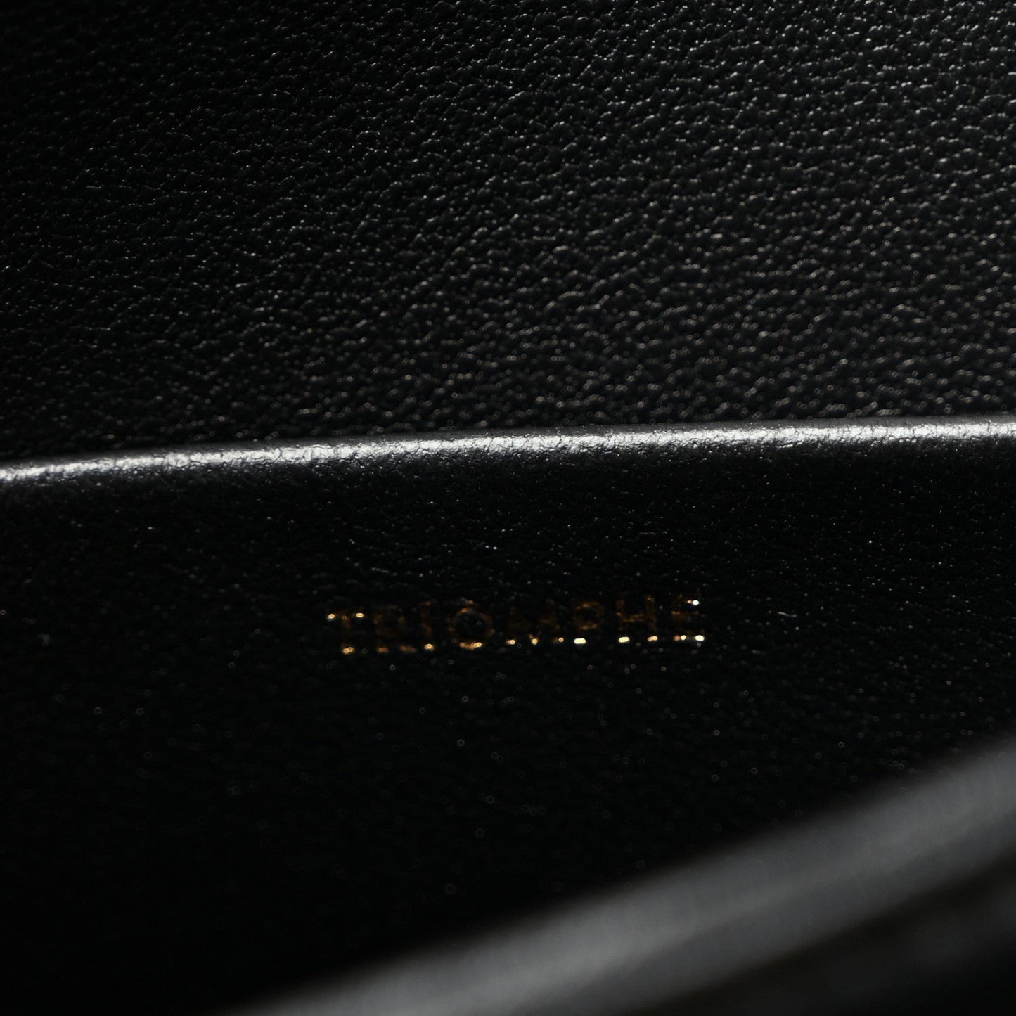 Close-up of black leather with faint embossed logo on bag panel.