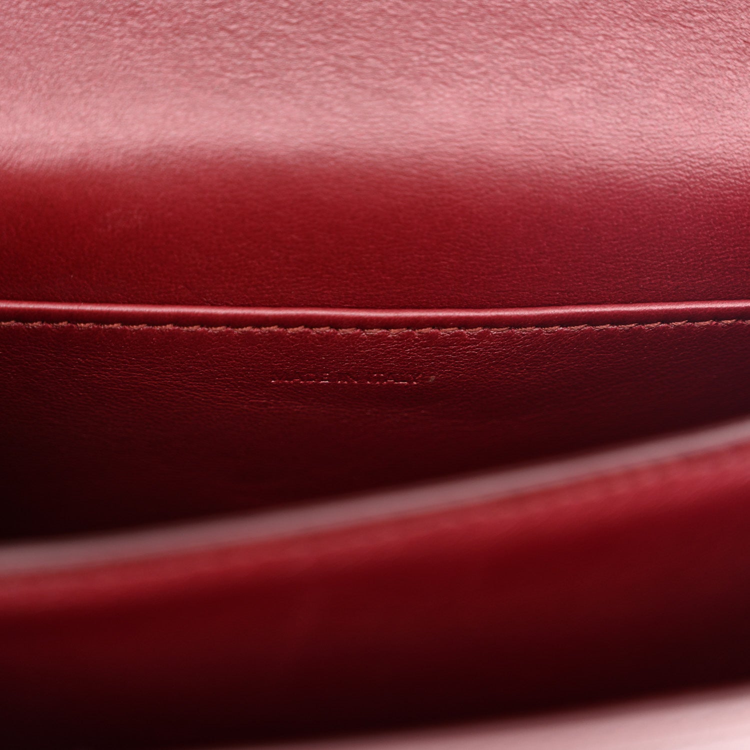 Burgundy leather lining edge detail with stitched seam inside a structured flap bag.
