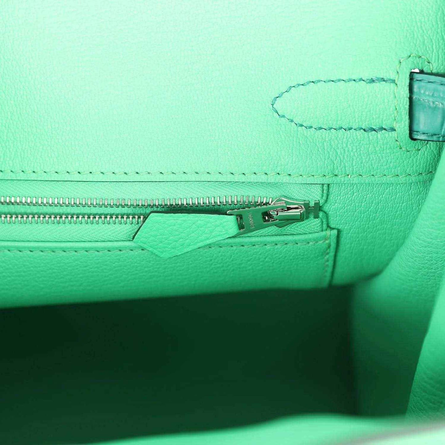 Elegant mint green leather handbag interior with a silver zipper, showcasing timeless design