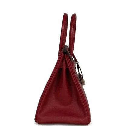 Elegant red leather handbag with structured silhouette and dual top handles, side view