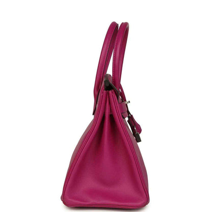 Elegant magenta leather handbag with structured silhouette and double handles, side view.
