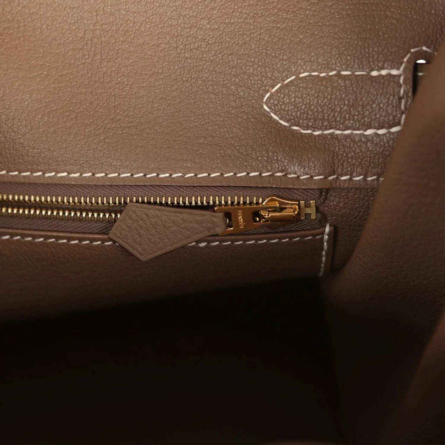 Elegant taupe leather handbag interior with gold zipper and white stitching, timeless style