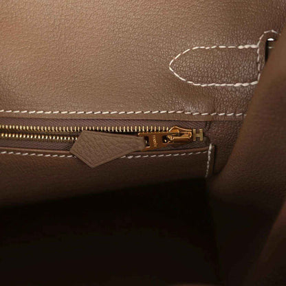 Elegant taupe leather handbag interior with gold zipper and white stitching, timeless style
