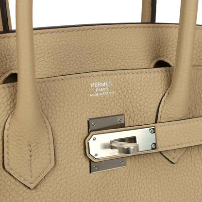 Elegant beige leather handbag with textured finish and polished silver hardware, timeless design