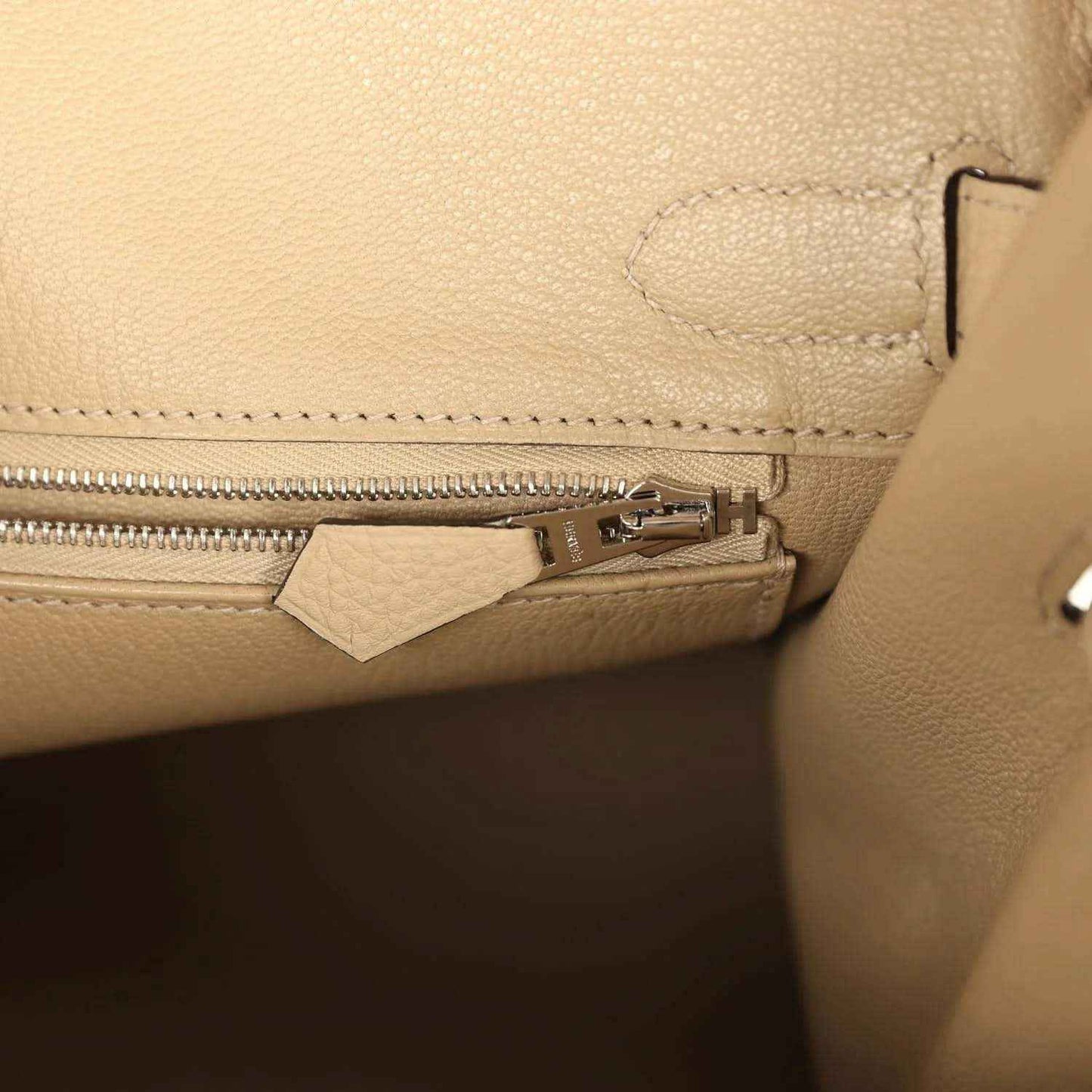 Close-up of a beige pebbled leather handbag with elegant silver zipper detailing