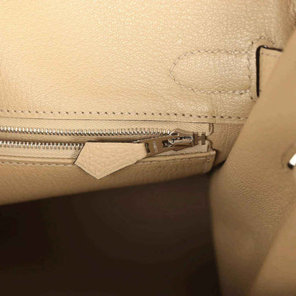 Close-up of a beige pebbled leather handbag with elegant silver zipper detailing
