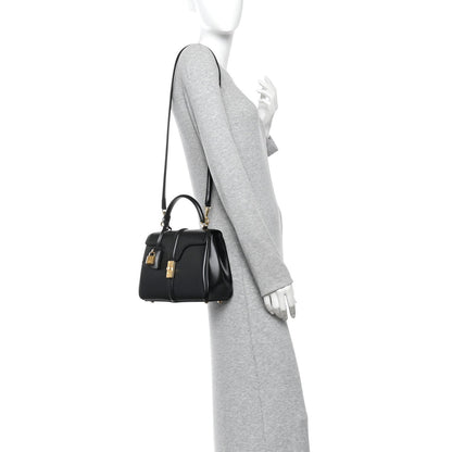 Black small top-handle bag on shoulder with gold-tone hardware and short strap
