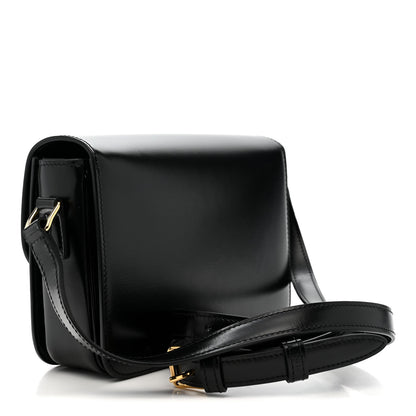 Black shiny leather crossbody bag with gold logo, flap front, and adjustable strap.