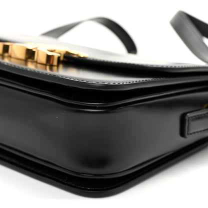 Close-up of black flap seam, white topstitching, and gold-tone hardware on strap.