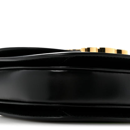 Black mini crossbody bag, close-up of smooth front panel and gold-tone trim